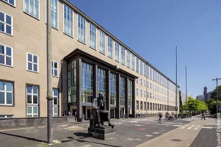 Universitäts-Hauptgebäude mit langer Fensterfront und Statue auf dem Vorplatz bei Sonnenschein
