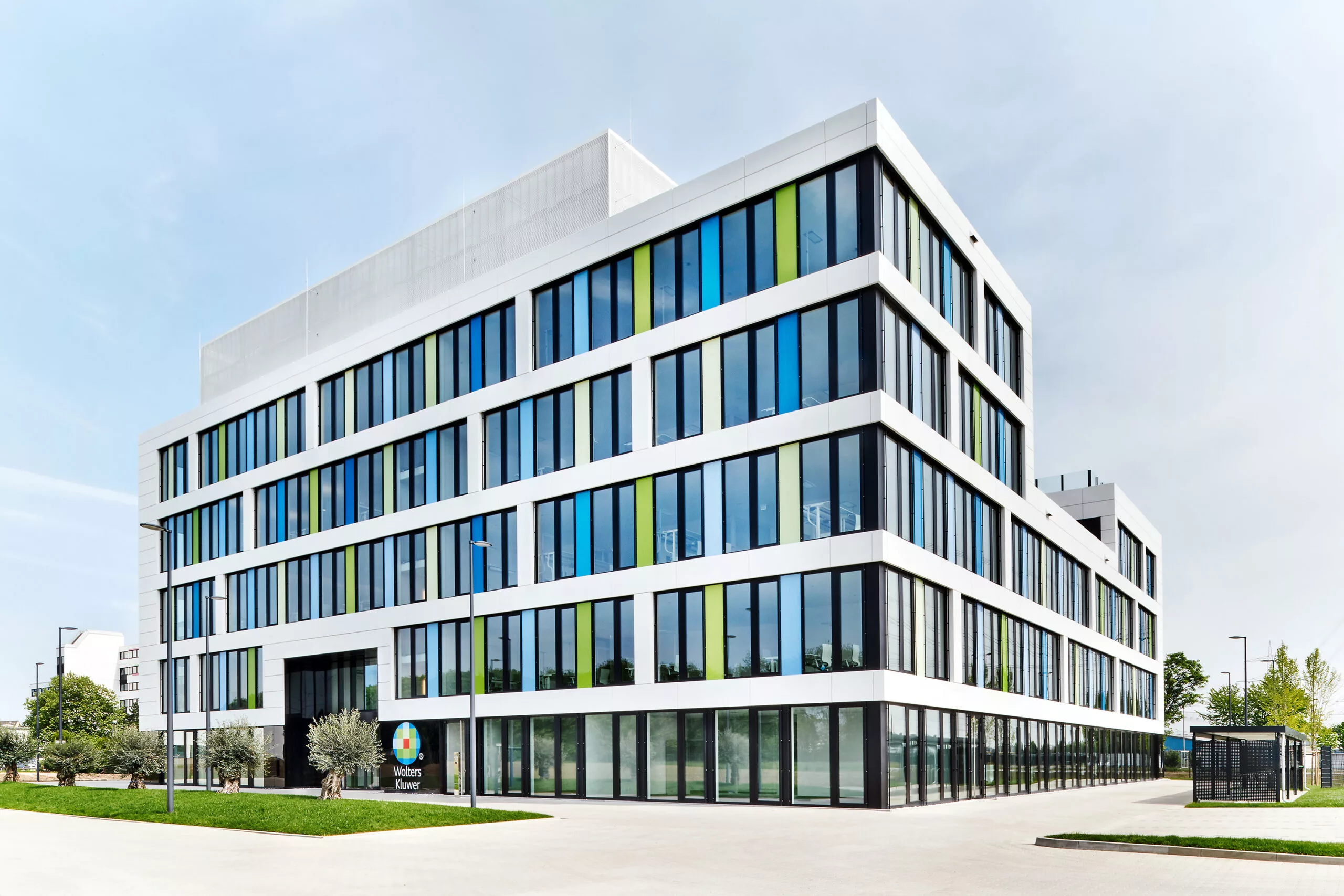 Wolters Kluwer Bürogebäude mit weißer Fassade, bunten Farbfeldern zwischen den Fenstern und verglastem Erdgeschoss.