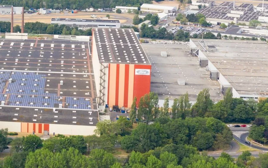 Luftaufnahme des Ford Werksgeländes mit langen Hallen, Photovoltaik auf den Dächern und Feldern ringsum