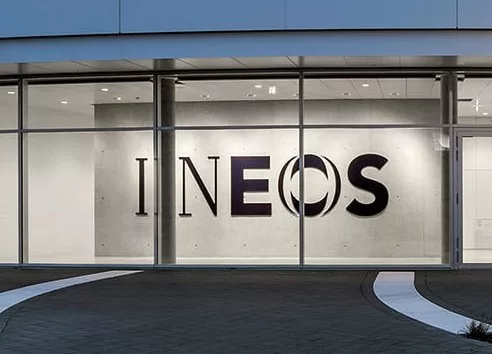 INEOS Gebäude in der Dämmerung: raumhoch verglaste Front mit Logo auf der Sichtbetonwand dahinter